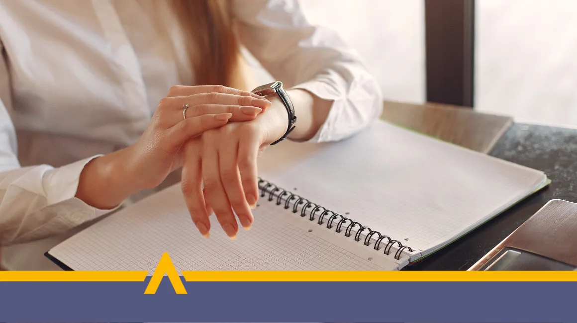 Kobieta sprawdzająca godzinę na zegarku przy biurku z otwartym zeszytem