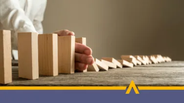 Ręka zatrzymująca przewracające się drewniane klocki na stole – symbol zatrzymania negatywnej reakcji łańcuchowej i zapobiegania konsekwencjom opóźnień w spłacie pożyczki.