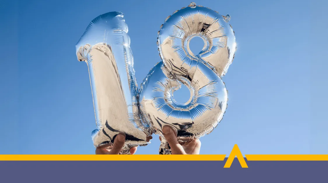 Srebrne balony w kształcie liczby 18 trzymane w dłoniach na tle błękitnego nieba, symbolizujące wejście w dorosłość